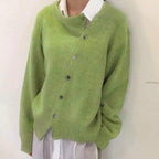 Cardigan vert asymétrique en laine, boutons décalés, porté sur chemise blanche. Mode automne-hiver, style décontracté et tendance.