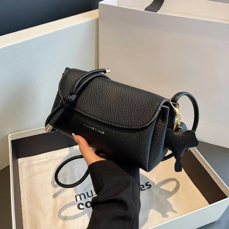 Sac à main en cuir noir texturé, design moderne, avec bandoulière et détails dorés, posé dans une boîte élégante. Accessoire mode tendance.