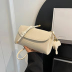 Sac à main blanc élégant en cuir texturé, avec fermeture à cordon et porte-clés en forme de chien, tenu par une main devant un fond noir et blanc.