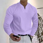 Homme en chemise violette, tenant un smartphone, debout devant une peinture moderne. Mode masculine, style décontracté, art contemporain.