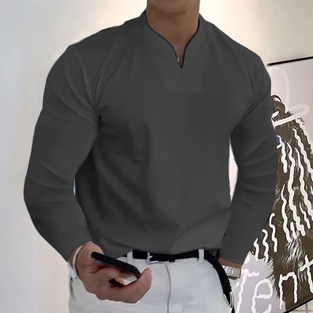 Homme en chemise grise élégante, tenant un smartphone, debout devant une peinture moderne. Mode masculine, style décontracté chic.