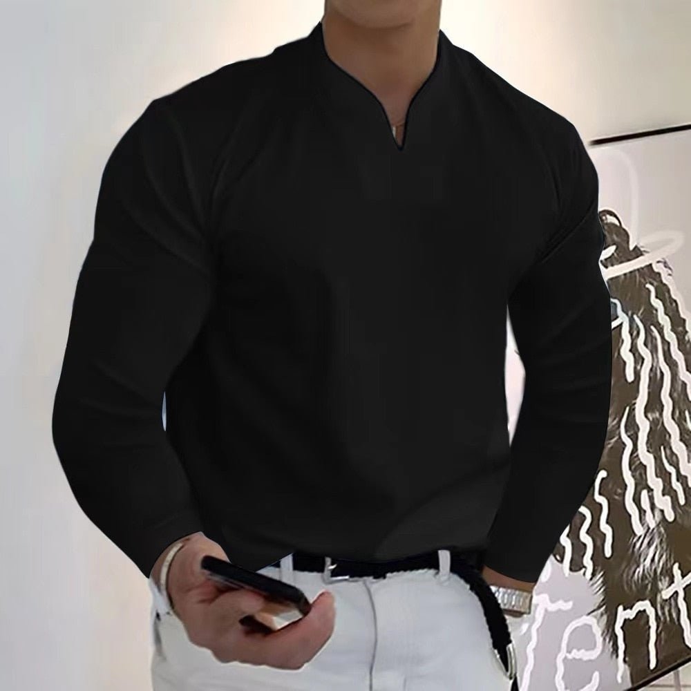 Homme en chemise noire élégante, manches longues, tenant un smartphone, debout devant une peinture moderne. Mode masculine, style décontracté.