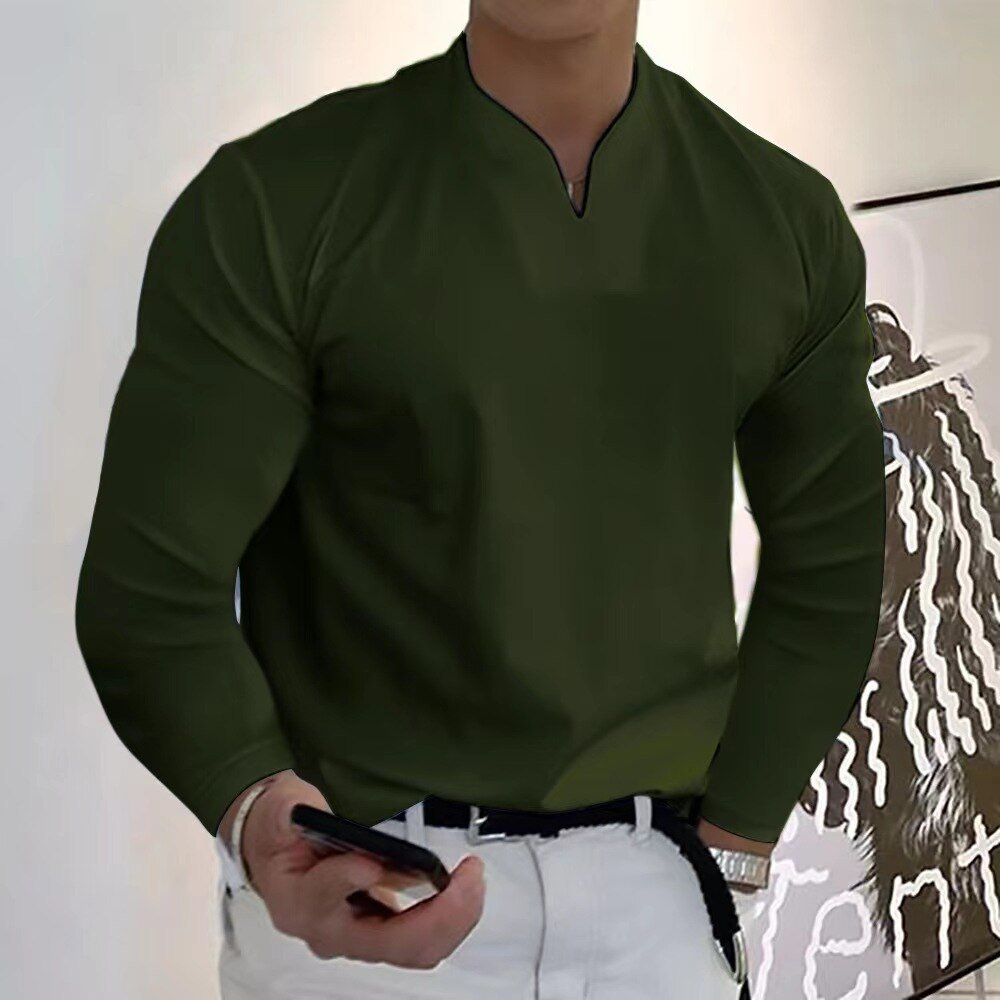 Homme en chemise verte à manches longues, tenant un smartphone, debout devant une peinture moderne. Mode masculine élégante et contemporaine.