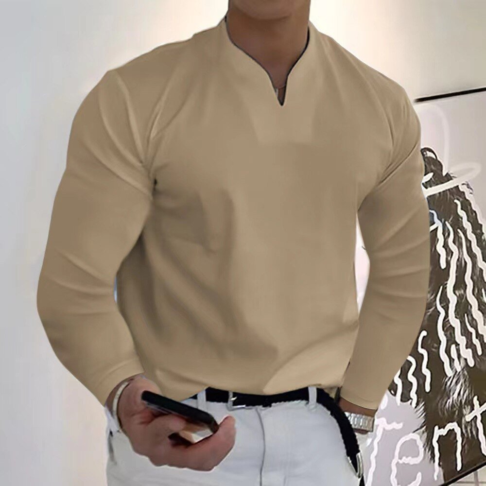 Homme en chemise beige élégante, tenant un smartphone, debout devant une peinture moderne. Mode masculine, style décontracté chic.
