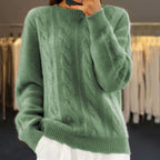 Pull vert en laine torsadée, manches longues, porté par une personne dans une boutique de vêtements. Mode automne-hiver, style décontracté et élégant.