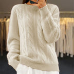 Pull en laine torsadé beige, manches longues, col rond, porté par une personne dans un magasin de vêtements. Mode automne-hiver, style décontracté.