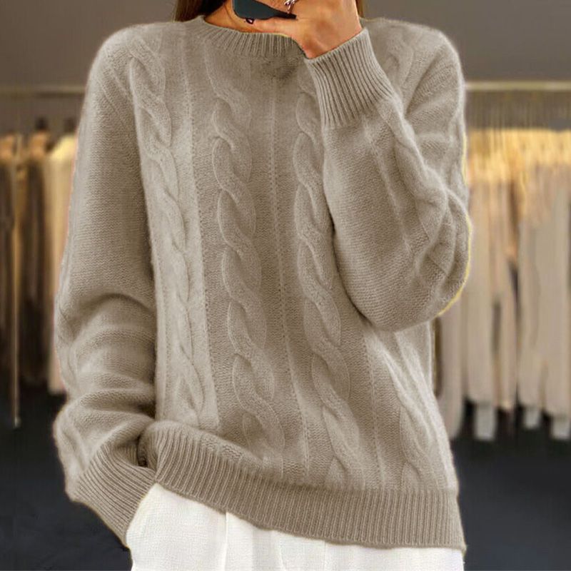 Femme portant un pull torsadé beige en laine, manches longues, col rond, dans une boutique de vêtements. Mode automne-hiver, style décontracté.