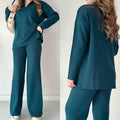 Femme portant un ensemble pull et pantalon bleu canard, style décontracté, avec sac beige. Mode automne-hiver, tenue confortable et élégante.