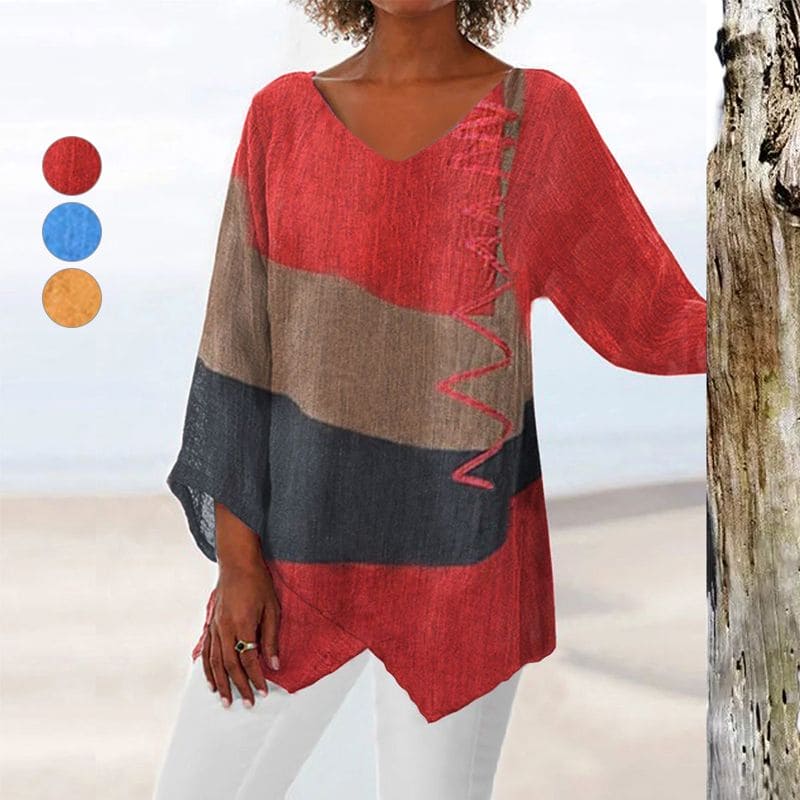 Femme portant un pull ample multicolore à manches longues, avec motifs rouges, bruns et noirs, sur fond de plage. Mode décontractée, style bohème.