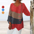 Femme portant un pull ample multicolore à manches longues, avec motifs rouges, bruns et noirs, sur fond de plage. Mode décontractée, style bohème.