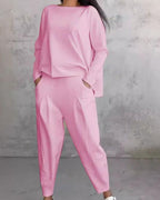 Tenue élégante rose pour femme, ensemble deux pièces avec haut ample et pantalon, style décontracté, fond gris minimaliste.