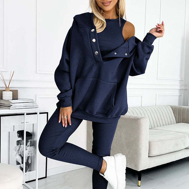 Femme en ensemble de survêtement bleu marine, style décontracté, avec épaules dénudées, posant dans un salon moderne. Mode féminine tendance.