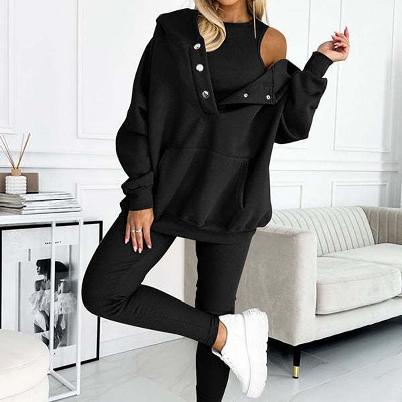 Femme portant un ensemble survêtement noir élégant, avec épaules dénudées et baskets blanches, dans un salon moderne. Mode décontractée chic.