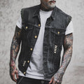 Homme tatoué portant un gilet en jean noir avec boutons dorés, sur un t-shirt blanc. Mode urbaine, style décontracté, tendance vestimentaire.