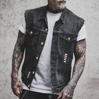 Homme tatoué portant un gilet en jean noir avec boutons dorés, sur un t-shirt blanc. Mode urbaine, style décontracté, tendance vestimentaire.