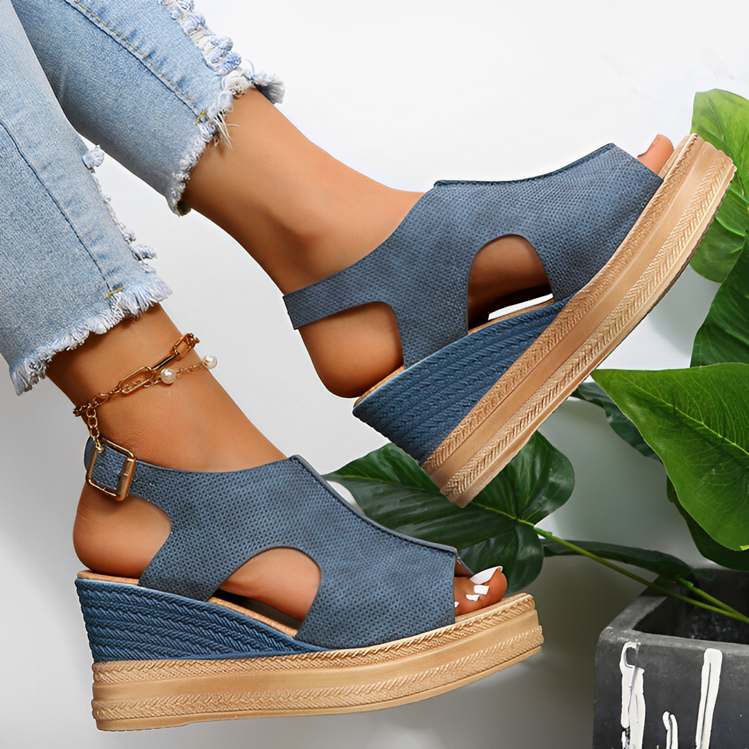 Sandales compensées bleues en cuir, portées avec un jean déchiré, posées sur fond de feuilles vertes. Mode estivale, chaussures tendance femme.