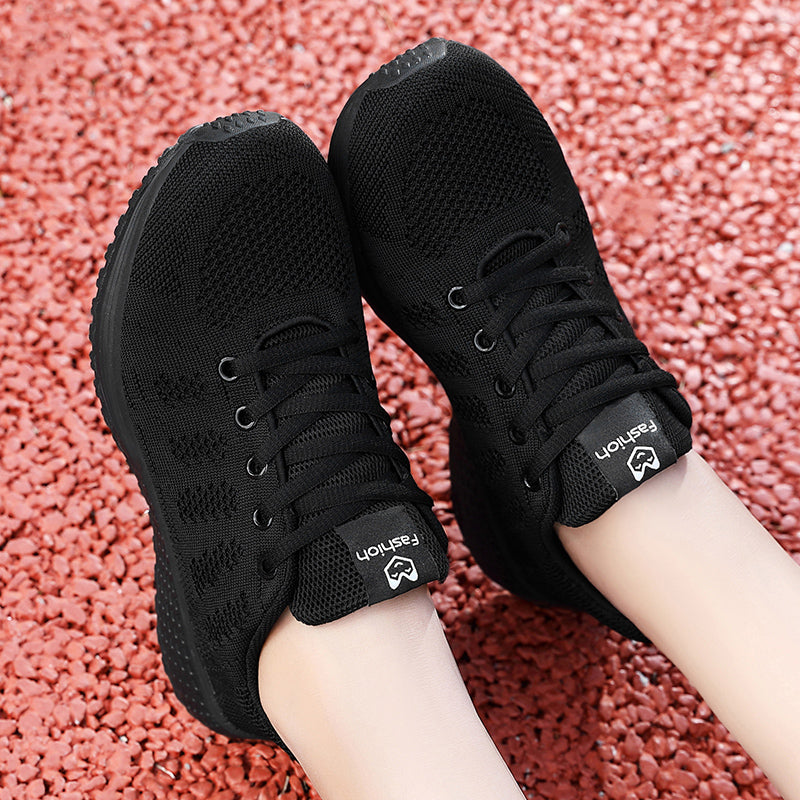 Chaussures de sport noires sur fond de gravier rouge, design respirant, lacets noirs, semelle antidérapante. Idéales pour la course et le fitness.