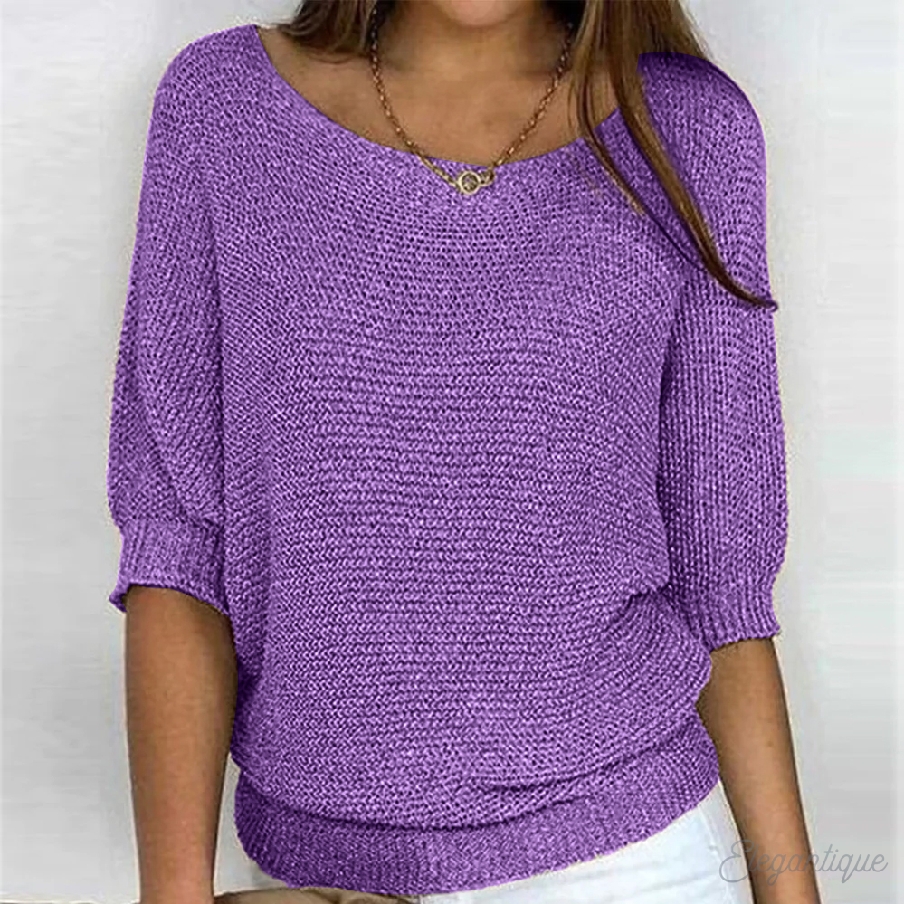 Femme portant un pull violet en tricot, manches trois-quarts, col bateau, avec un collier doré. Mode féminine, tendance automne-hiver.
