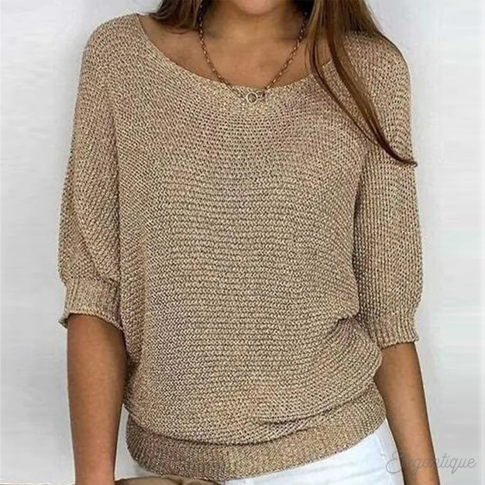 Femme portant un pull beige en maille, manches trois-quarts, col rond, avec un collier doré, sur fond blanc. Mode féminine élégante et décontractée.