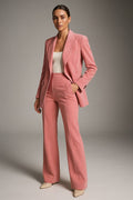 Femme portant un costume rose élégant, veste et pantalon assortis, sur fond neutre. Mode féminine, tenue professionnelle chic, style moderne.