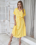 Robe jaune à pois blancs, manches courtes, portée par une femme souriante. Mode estivale élégante, tendance et décontractée.