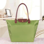 Sac à main vert en toile avec poignées en cuir marron, posé sur une table. Accessoire de mode élégant pour femme, idéal pour le quotidien.