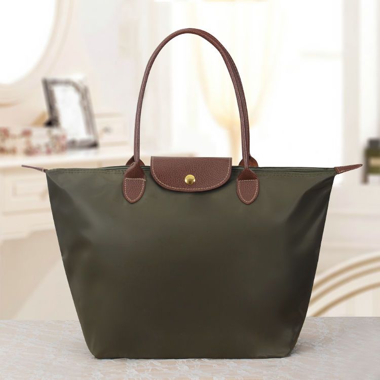 Sac à main en toile vert olive avec poignées en cuir marron, posé sur une table. Accessoire mode élégant et pratique pour femme.