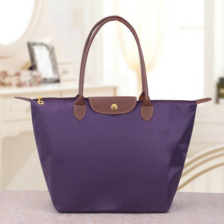 Sac à main violet élégant avec poignées en cuir marron, posé sur une table. Accessoire de mode chic pour femmes, idéal pour le quotidien.