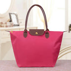Sac à main rose vif avec poignées marron, posé sur une table. Design élégant et moderne, idéal pour la mode féminine et les accessoires tendance.
