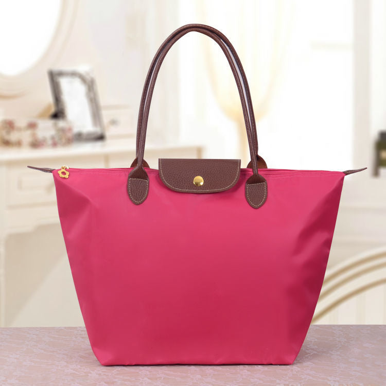 Sac à main rose vif avec poignées marron, posé sur une table. Design élégant et moderne, idéal pour la mode féminine et les accessoires tendance.