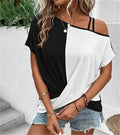 Femme portant un t-shirt bicolore noir et blanc, épaules dénudées, avec des bijoux dorés et un short en jean, posant devant un mur blanc.