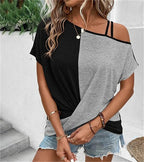 Femme portant un t-shirt bicolore noir et gris, épaules dénudées, avec des bijoux dorés et un short en jean, posant devant des plantes vertes.