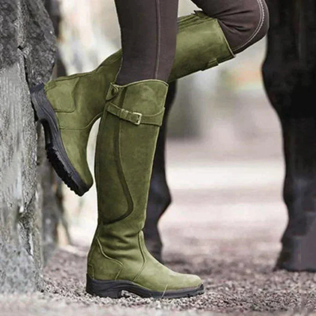 Bottes d'équitation vertes en daim pour femme, avec semelles antidérapantes, portées en extérieur sur un sol gravillonné.