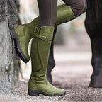 Bottes d'équitation vertes en daim pour femme, avec semelles antidérapantes, portées en extérieur sur un sol gravillonné.