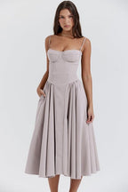 Robe midi élégante beige avec bretelles fines, corsage ajusté et jupe évasée, portée par une femme sur fond blanc. Mode féminine chic.