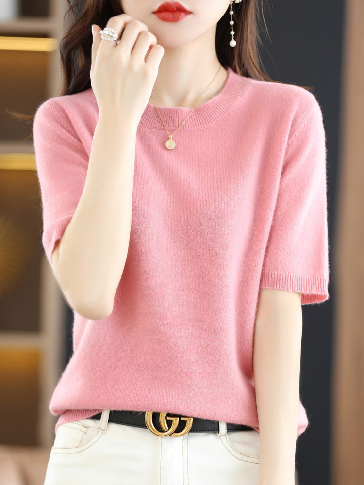 Femme portant un pull rose en cachemire, collier doré et boucle d'oreille, ceinture noire avec boucle dorée, style élégant et moderne.