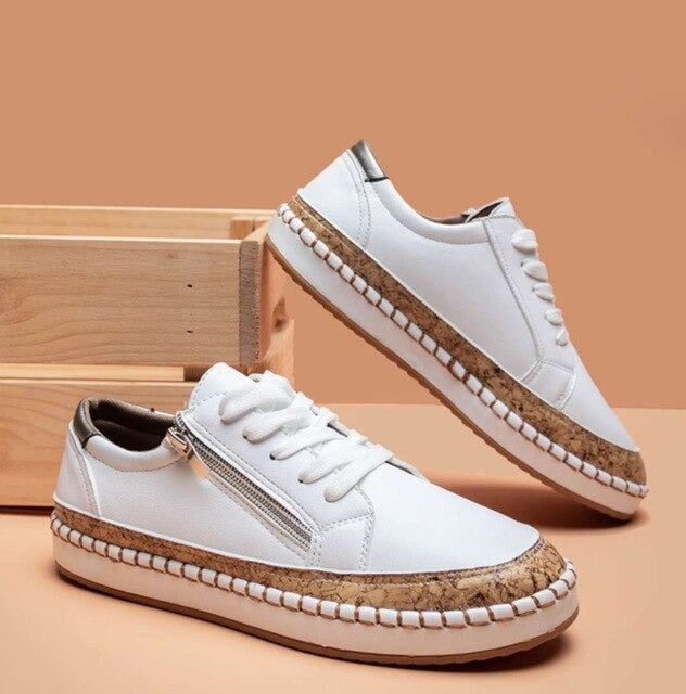 Chaussures blanches en cuir avec semelle en liège, fermeture éclair latérale, posées sur fond beige. Sneakers tendance pour femmes.