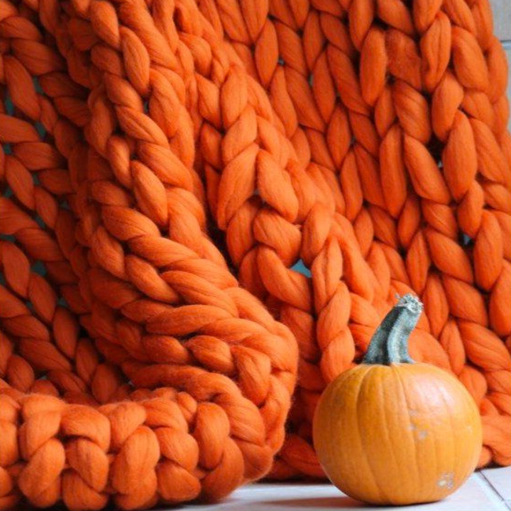 Couverture en tricot épais orange avec une petite citrouille. Décoration automnale, texture douce, ambiance chaleureuse.