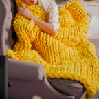 Personne enveloppée dans une couverture en laine jaune épaisse sur un canapé, confort et chaleur, décoration intérieure moderne, relaxation à la maison.