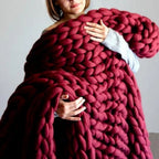 Femme tenant une couverture en laine épaisse bordeaux, tricotée à la main, idéale pour décoration intérieure et confort hivernal.