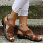 Sandales marron en cuir pour femme avec talon compensé, portées avec un pantalon blanc déchiré, posées sur des marches en pierre.