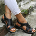 Sandales noires en cuir pour femme avec talon compensé, portées avec un jean blanc déchiré, sur fond de marches en pierre.