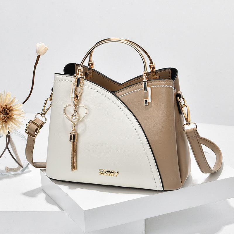 Sac à main en cuir bicolore beige et blanc avec poignée dorée, bandoulière amovible, et porte-clés cœur. Accessoire mode élégant pour femme.