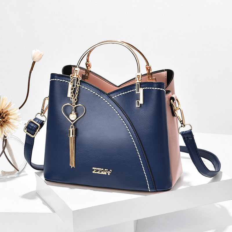 Sac à main en cuir bleu et rose avec bandoulière, orné d'un pendentif cœur doré. Élégant et moderne, idéal pour la mode féminine.