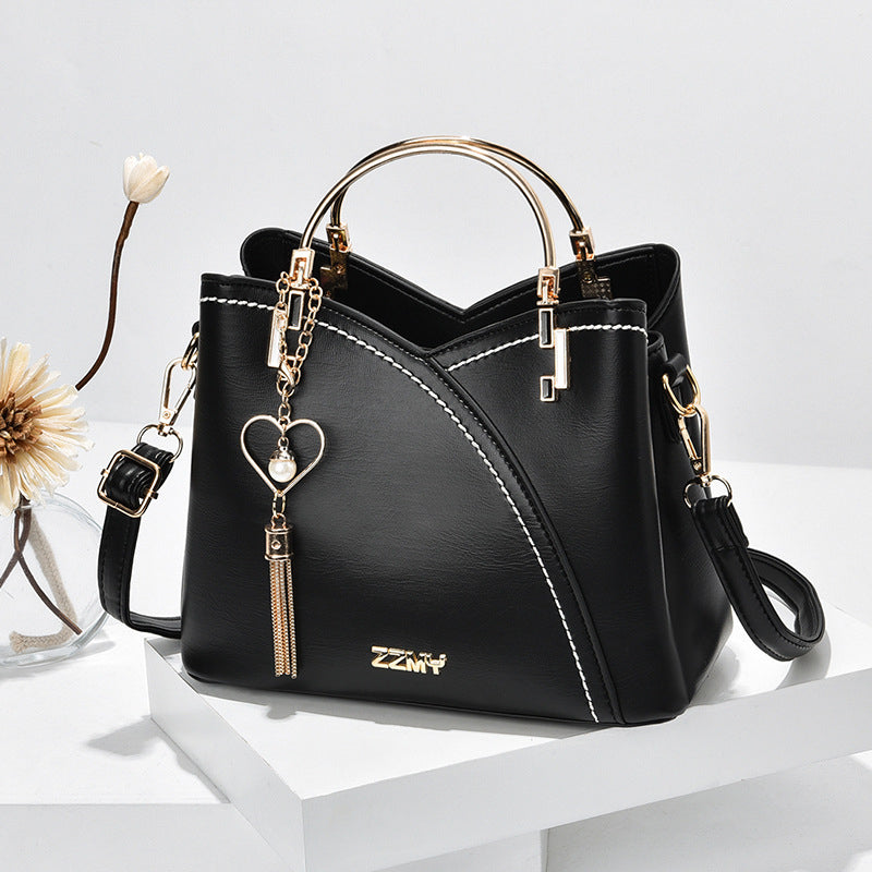 Sac à main noir élégant avec poignées dorées, bandoulière amovible, pendentif cœur et coutures blanches. Accessoire mode femme chic et moderne.