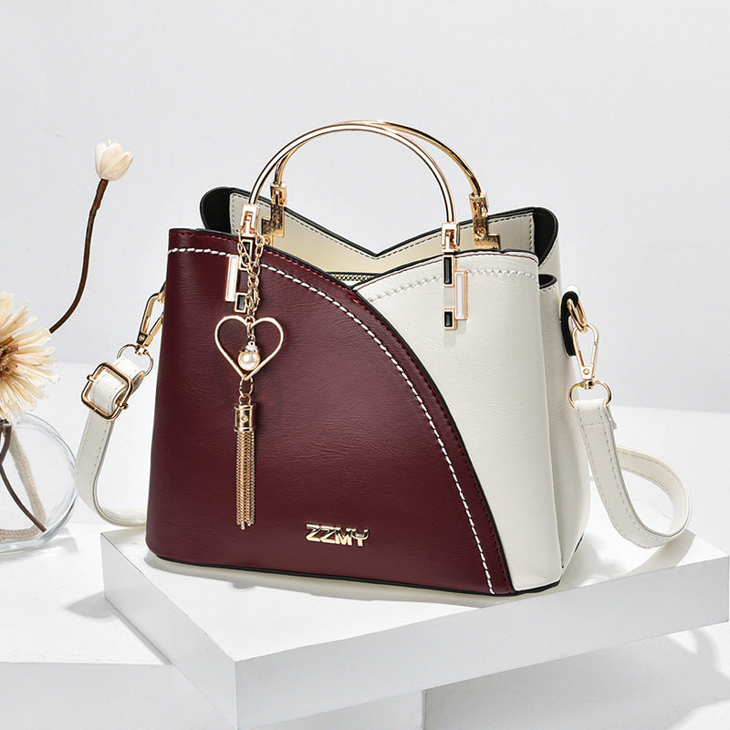 Sac à main bicolore en cuir blanc et bordeaux avec poignée dorée, bandoulière amovible et pendentif cœur. Accessoire mode élégant et tendance.